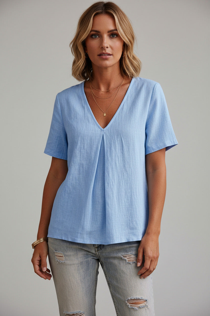 Woman wearing a light blue shirt and jeans against a dark wall.