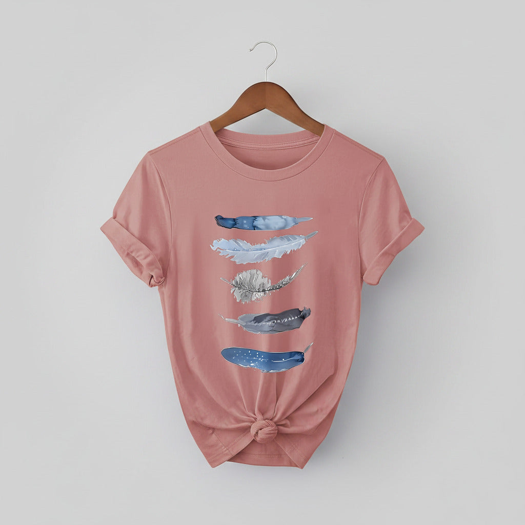 Pink t-shirt with feather designs on a hanger against a denim background